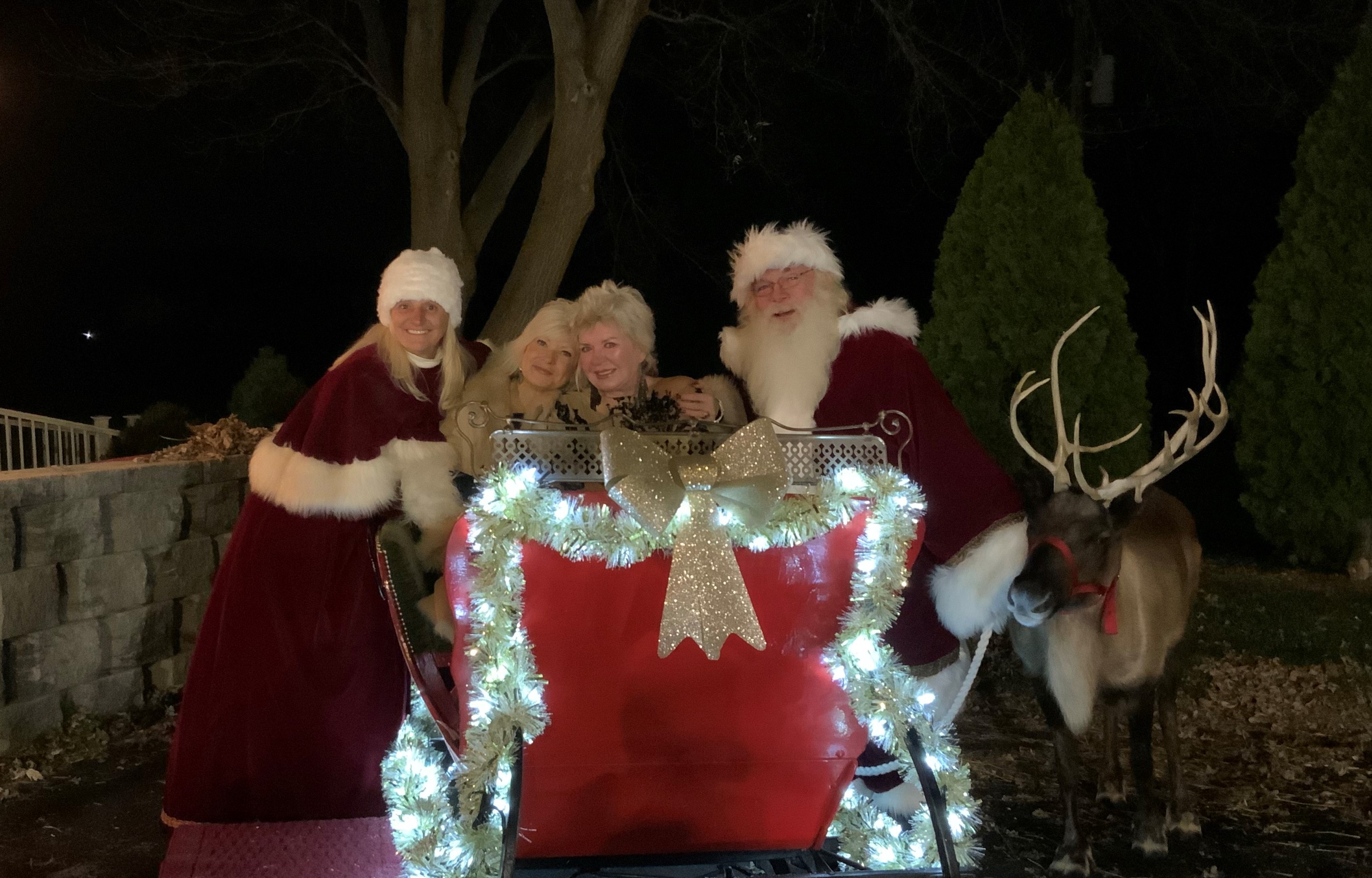 Two people dressed as Santa and Mrs. Claus stand beside a red sleigh